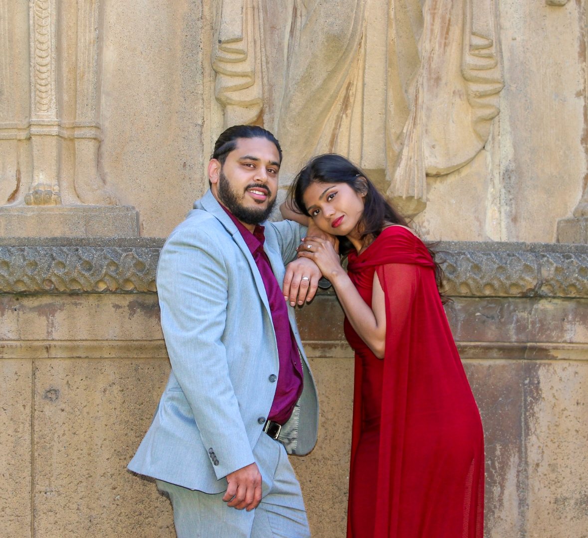 Prunella and Johnetan leaning together against a carved stone wall